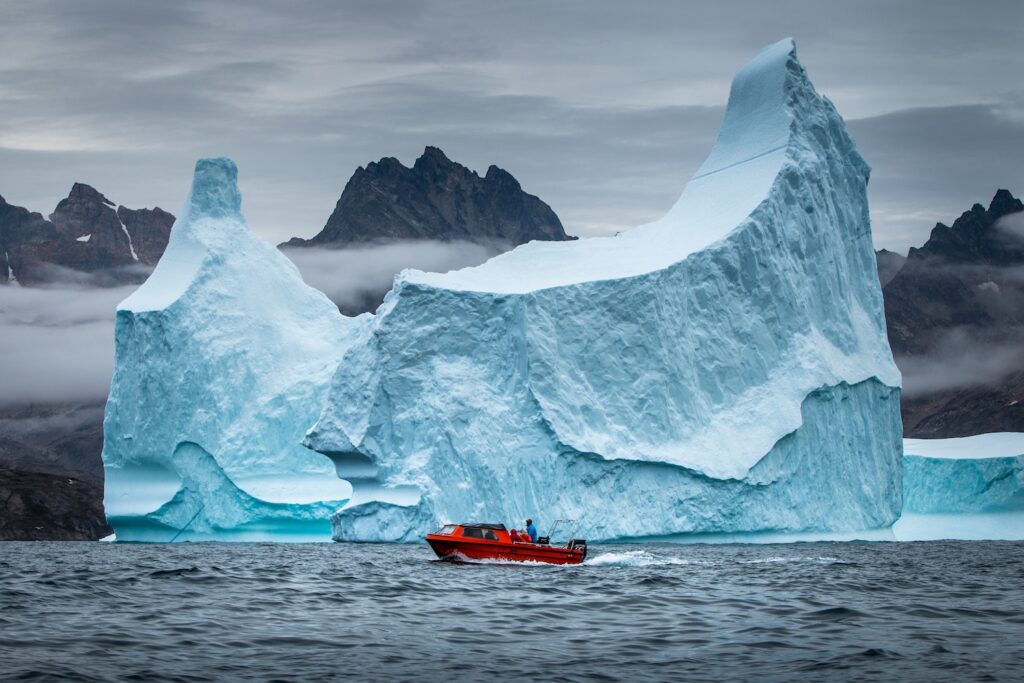 Barco vermelho diante de um imenso iceberg