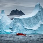 Barco vermelho diante de um imenso iceberg
