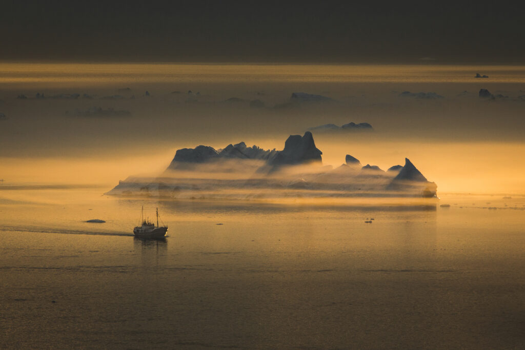 A fishing vessel passing an iceberg shrouded in fog near Ilulissat ice fjord in Greenland