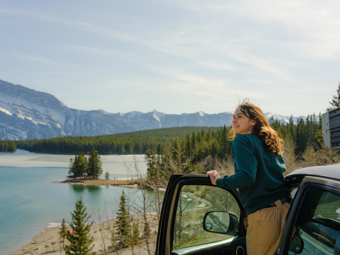 Woman looking at scenic lake in Banff during road trip with SUV in springtime