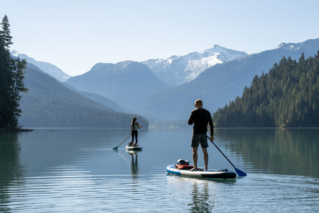 Couple paddle SUP boards across mountain lake, Whistler