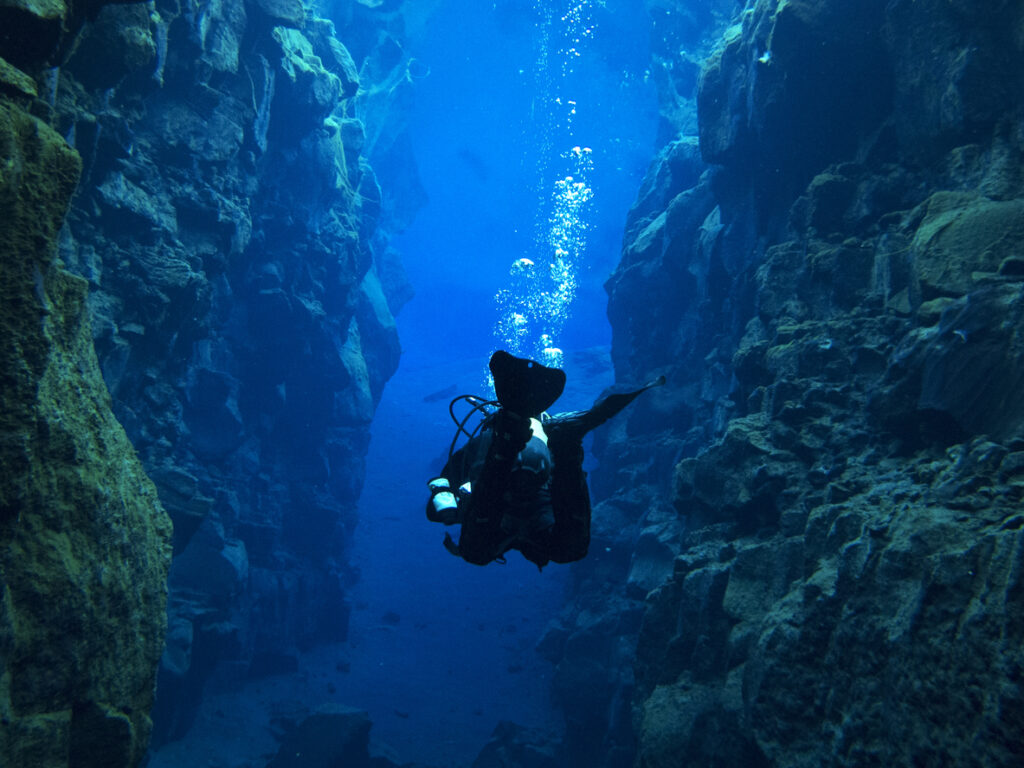 View from Behind Single Scuba Diver with Bubbles Above at Continental Split at Silfra in Deep Section at Pingvellir National Park