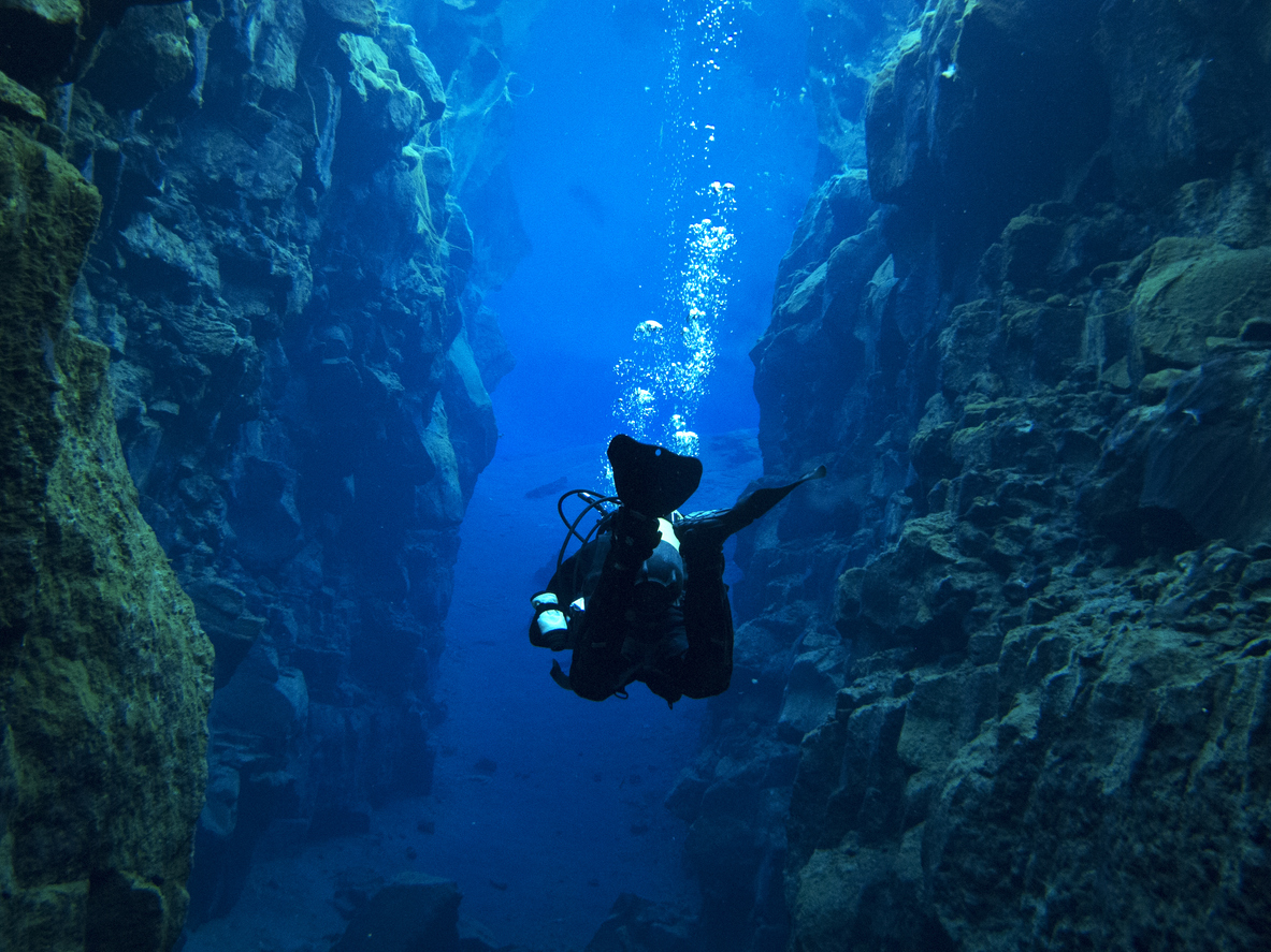 View from Behind Single Scuba Diver with Bubbles Above at Continental Split at Silfra in Deep Section at Pingvellir National Park