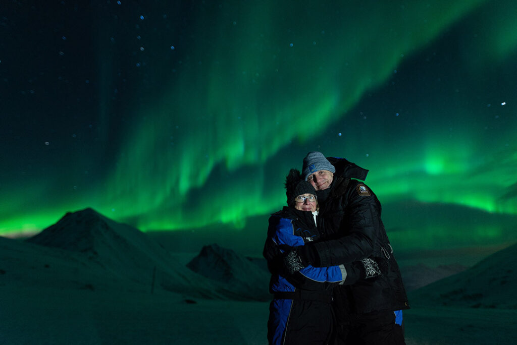 Casal se abraça em frente à Aurora Boreal