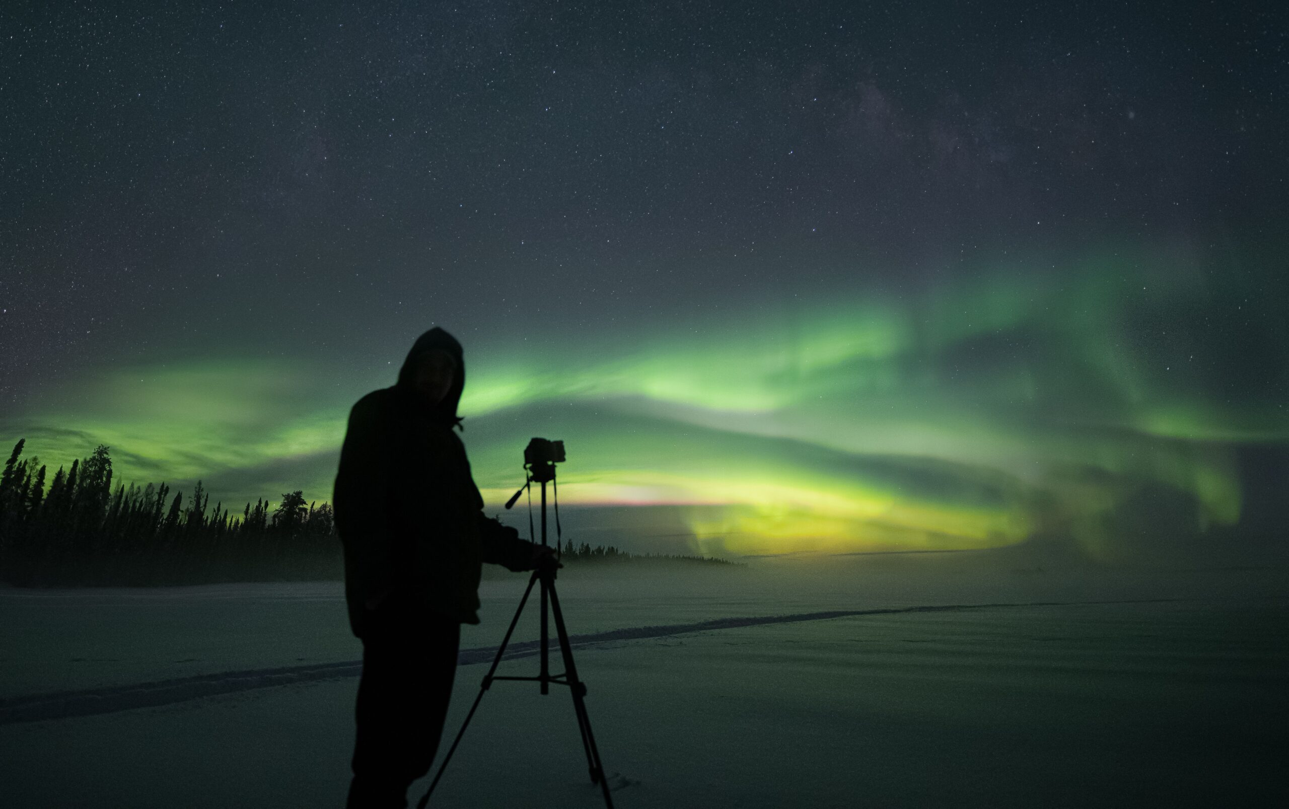 Homem posando ao lado de câmera, pronto para fotografar a Aurora Boreal