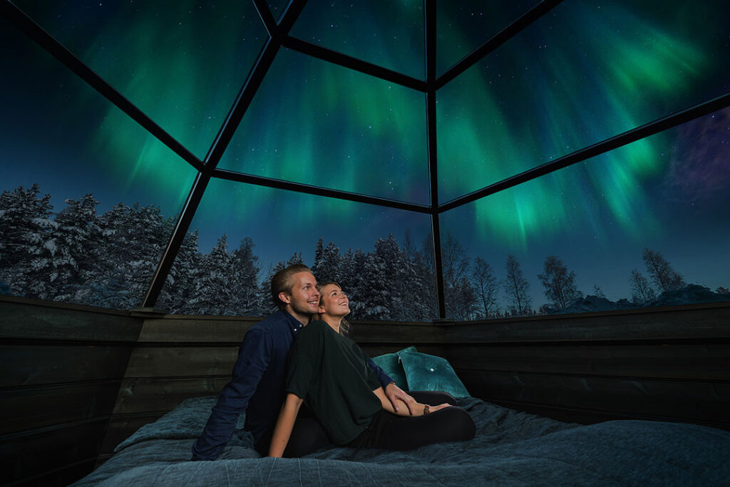 Casal vendo a Aurora Boreal sob um Iglu de Vidro, em Rovaniemi na Finlândia